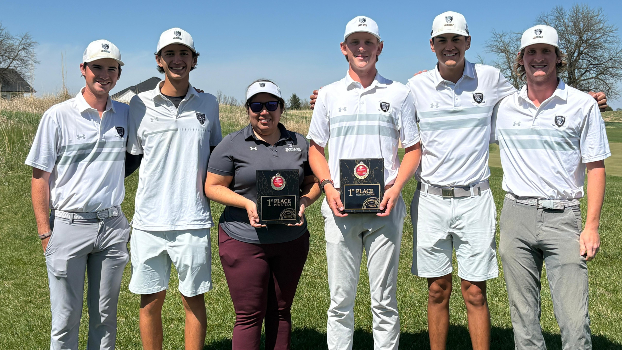 The men's golf team poses with Coach Cano displaying championship hardware. 